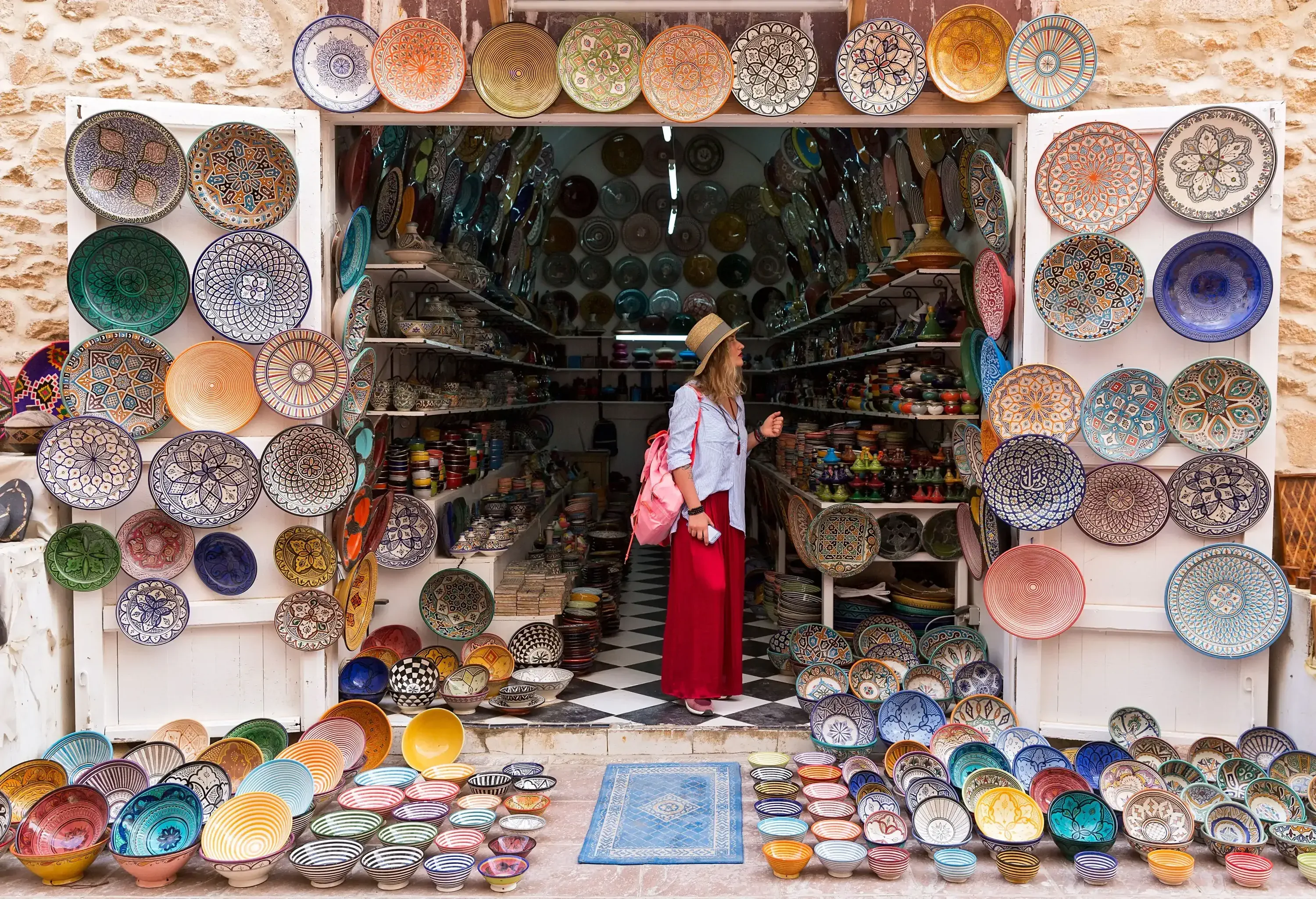 A woman standing in the aisle of a store with a vast display of decorative plates in various designs.