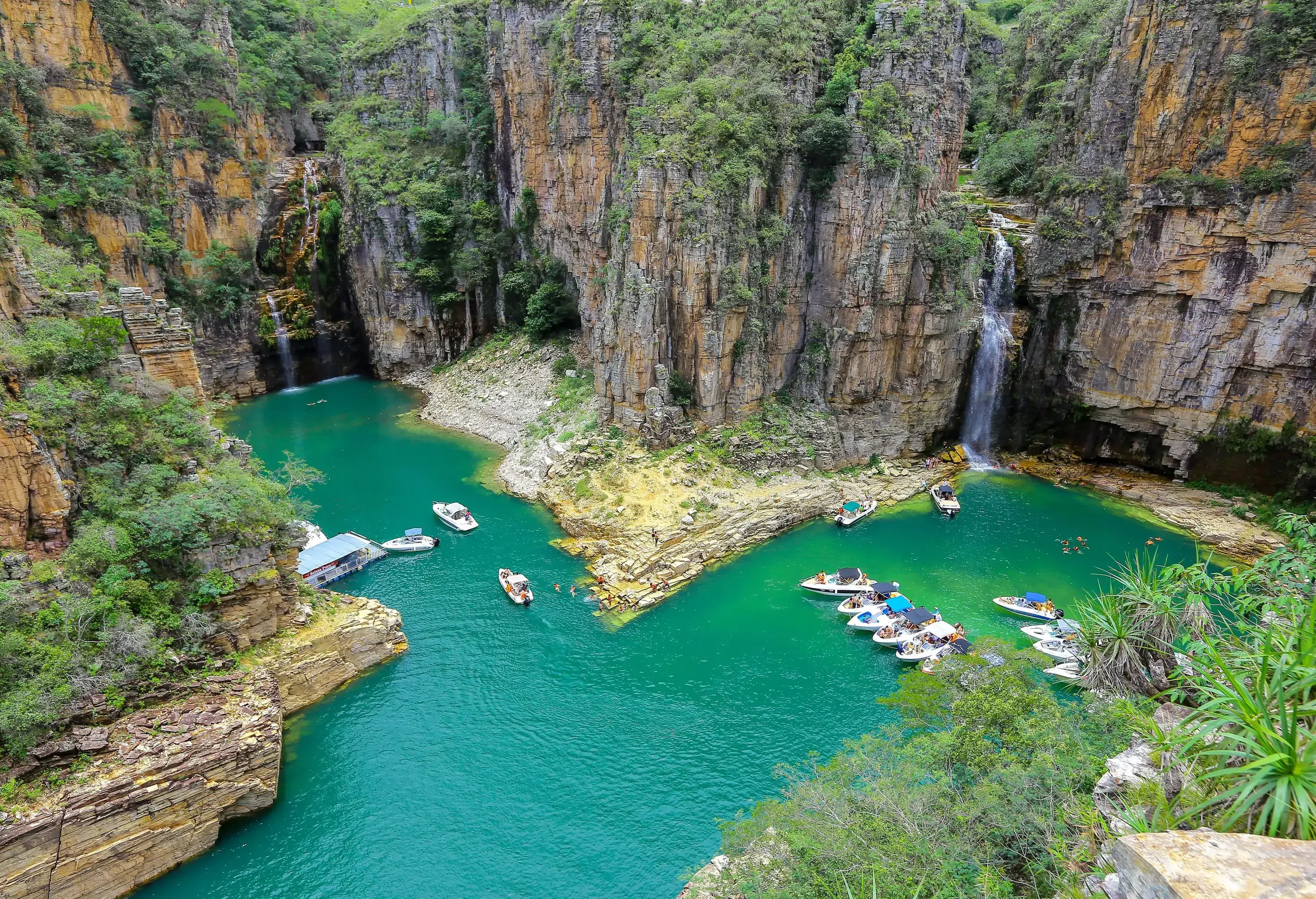 Furnas Canyon, a lush haven with boats moored on the tranquil lake below, surrounded by verdant vegetation and adorned with cascading waterfalls.