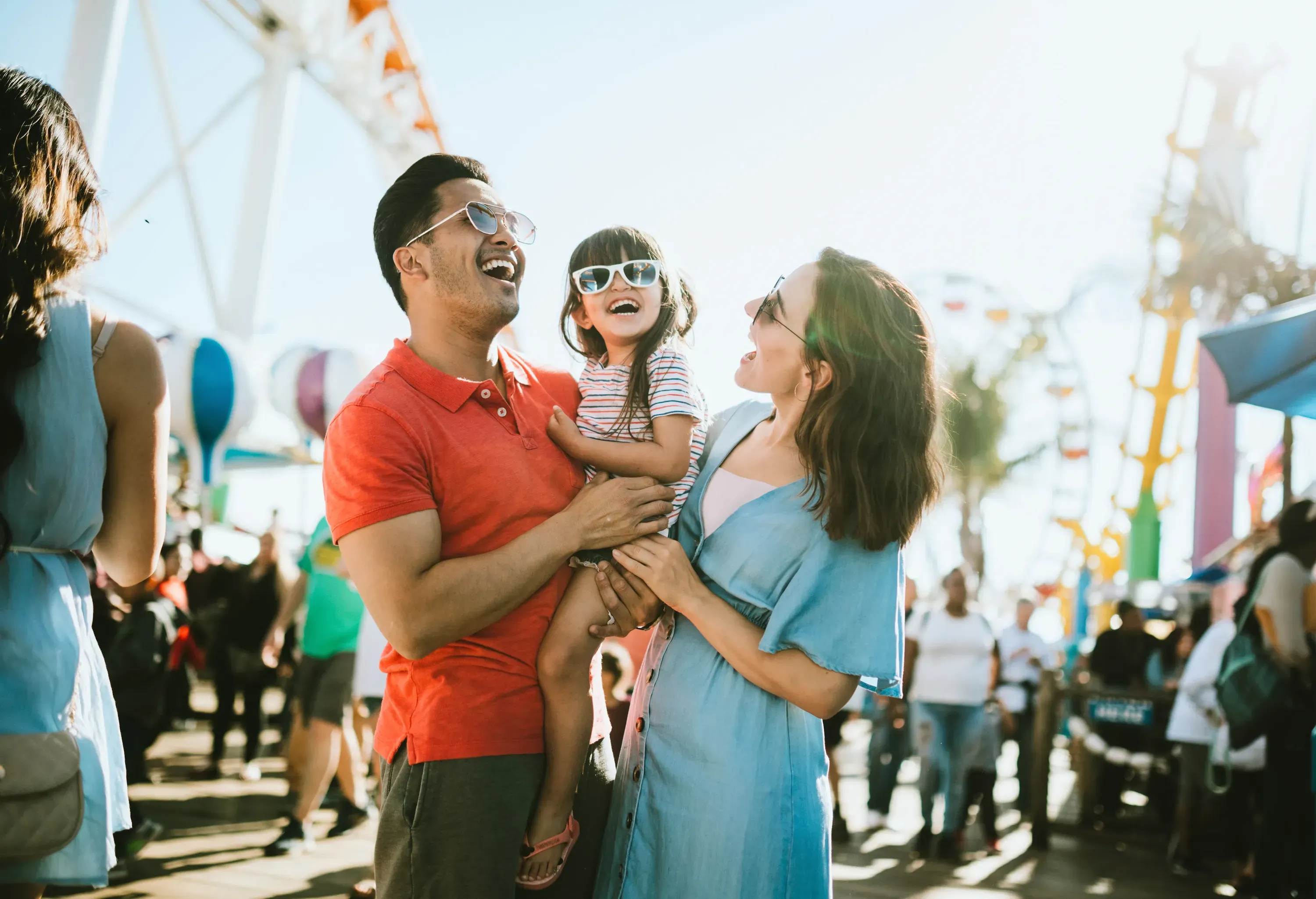A cute mixed race family enjoys the rides and sun at the fair activities on Santa Monica Pier in Los Angeles, California. They all wear sunglasses with big smiles.