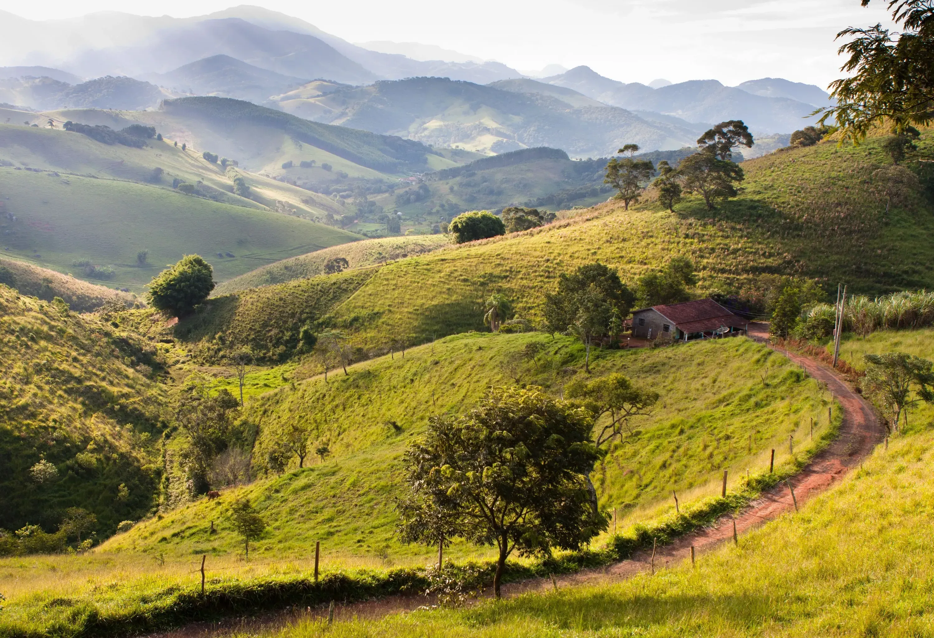 A dirt road across a grassy hill towards a house with views of misty rolling hills.