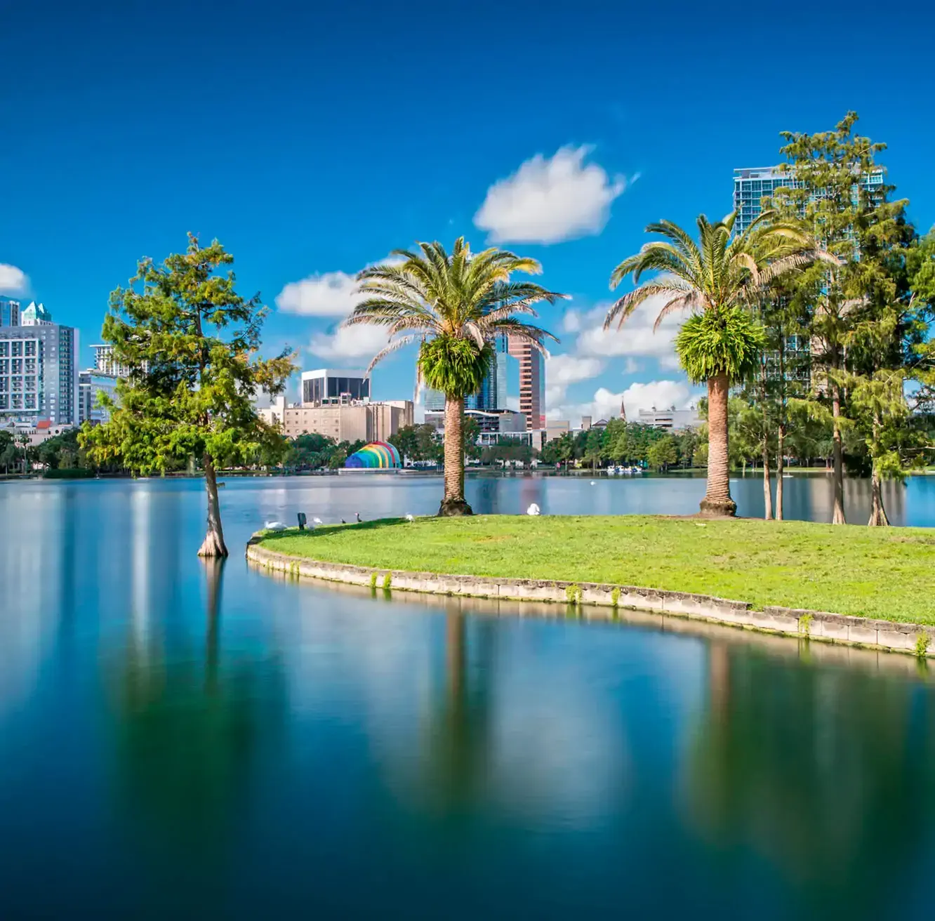Sunny day at Lake Eola Park in downtown Orlando, featuring palm trees and city skyline views.