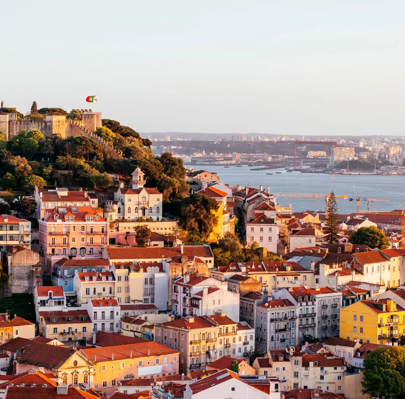 Colorful hillside view of Lisbon with São Jorge Castle and the Tagus River in the background.