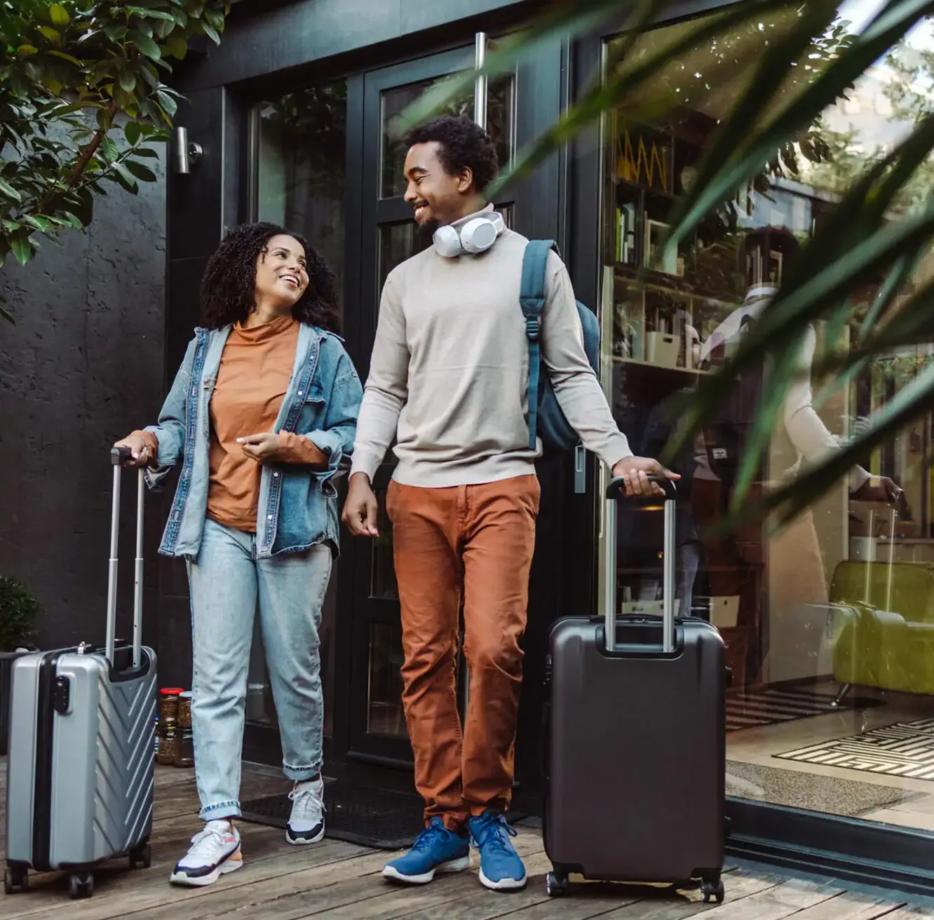 Happy couple leaving their hotel with suitcases, ready to explore their next destination.