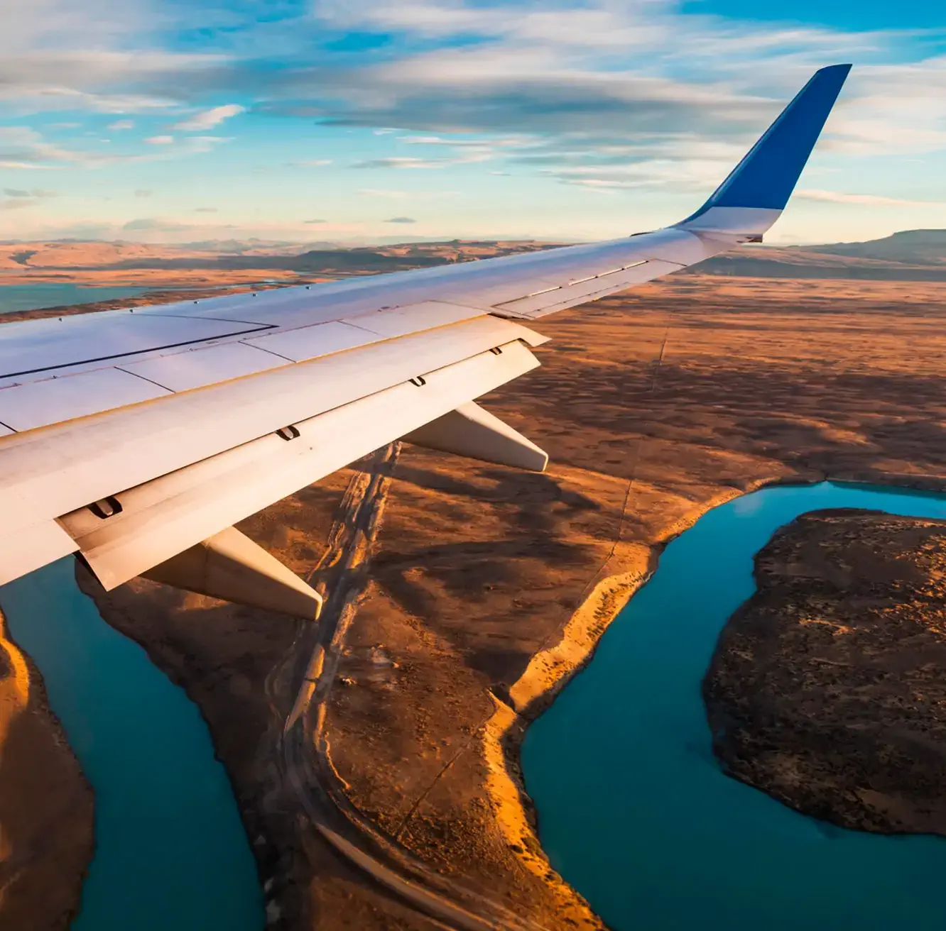 Aerial view of winding river and desert landscape seen from an airplane window during golden hour.