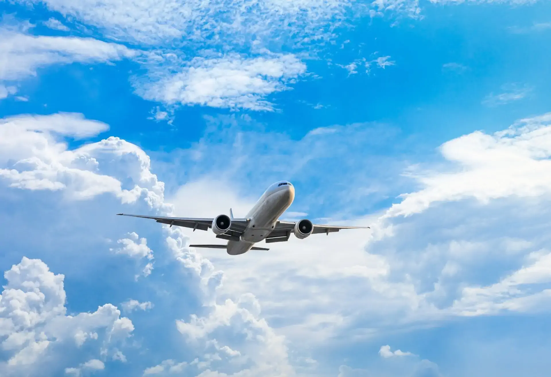 Avião comercial em ascensão entre nuvens brancas e céu azul, simbolizando o início de uma nova viagem aérea.