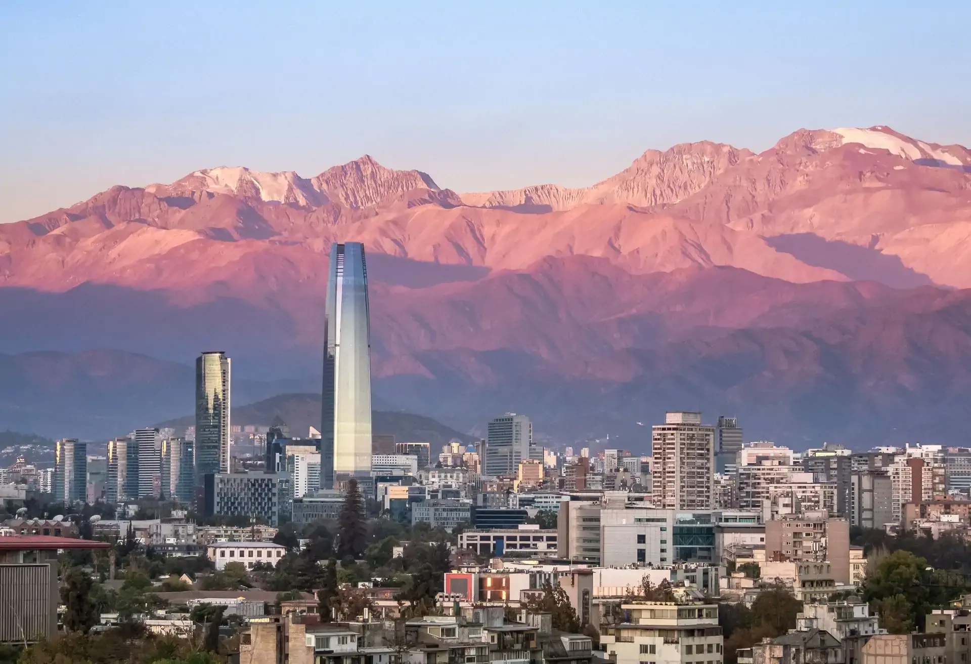 Vista panorâmica da cidade com arranha-céus e montanhas cobertas por tons rosados ao entardecer em Santiago.
