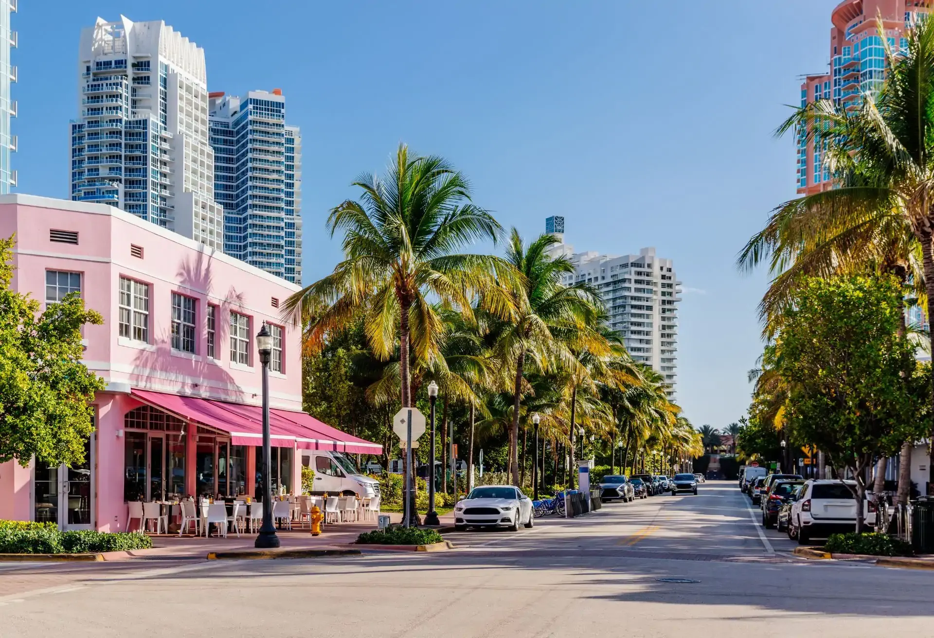 Avenida com prédios art déco, palmeiras altas e carros estacionados, representando uma rua icônica de Miami.